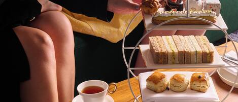 A table set with a variety of sandwiches, scones, and pastries, along with a cup of tea.