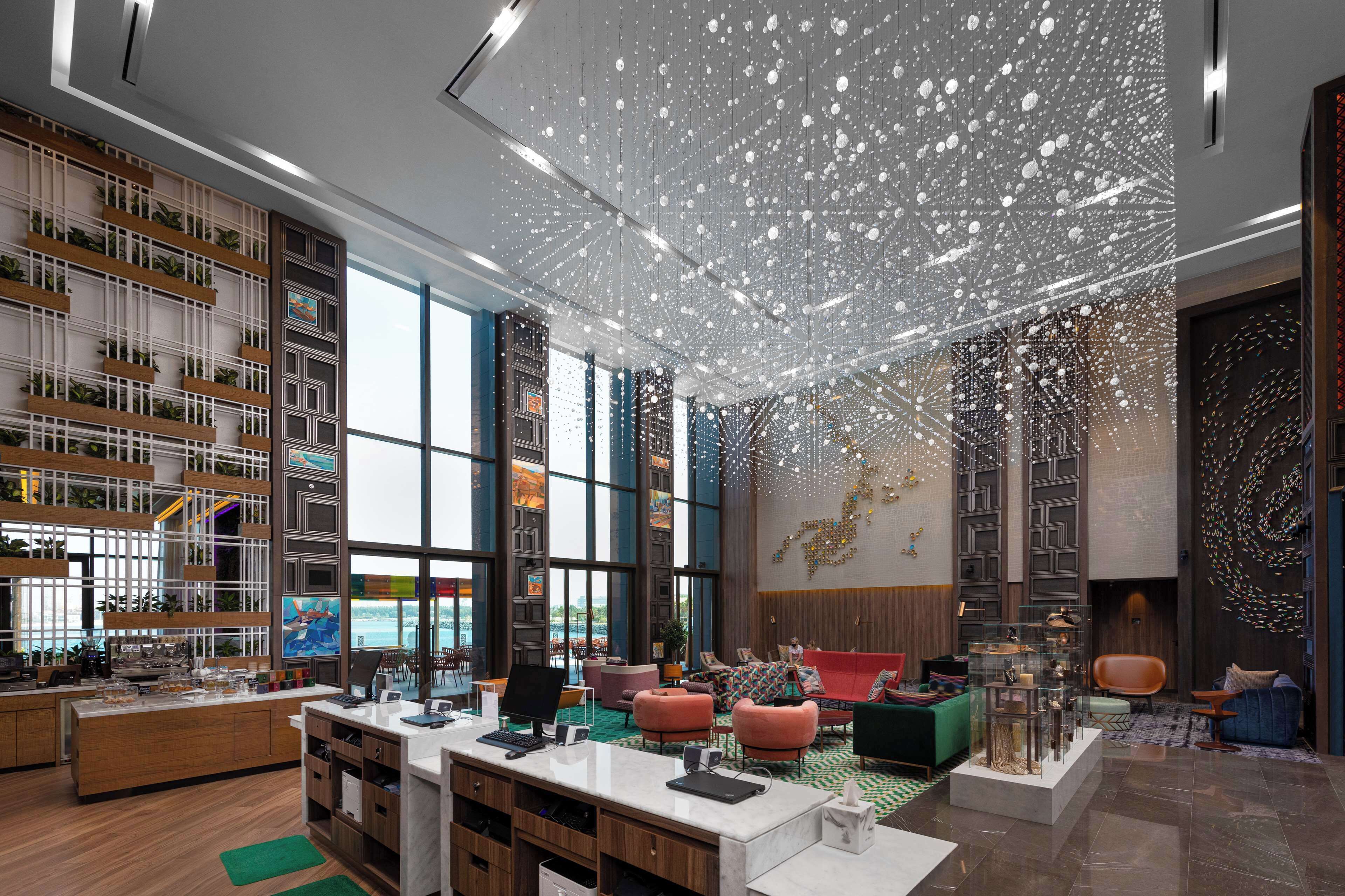 A modern hotel lobby with a reception desk, seating areas, and a large window offering a view.