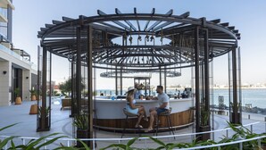 A circular outdoor seating area with a bar, surrounded by potted plants and overlooking a body of water. - Hyatt Centric Jumeirah Dubai (Dubai)