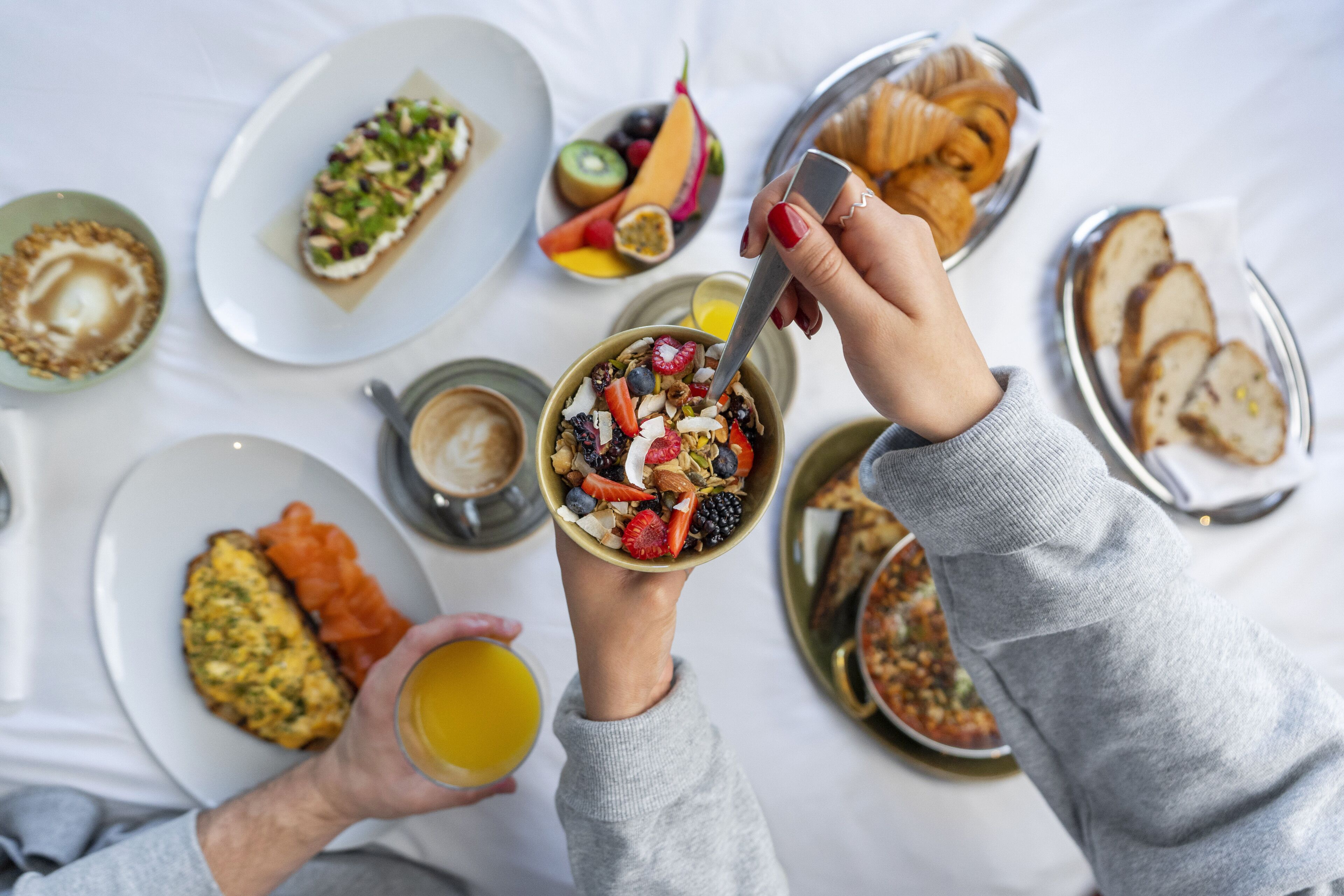 Une table mise pour le petit-déjeuner, avec différents plats, notamment des toasts, des fruits et un bol de céréales.