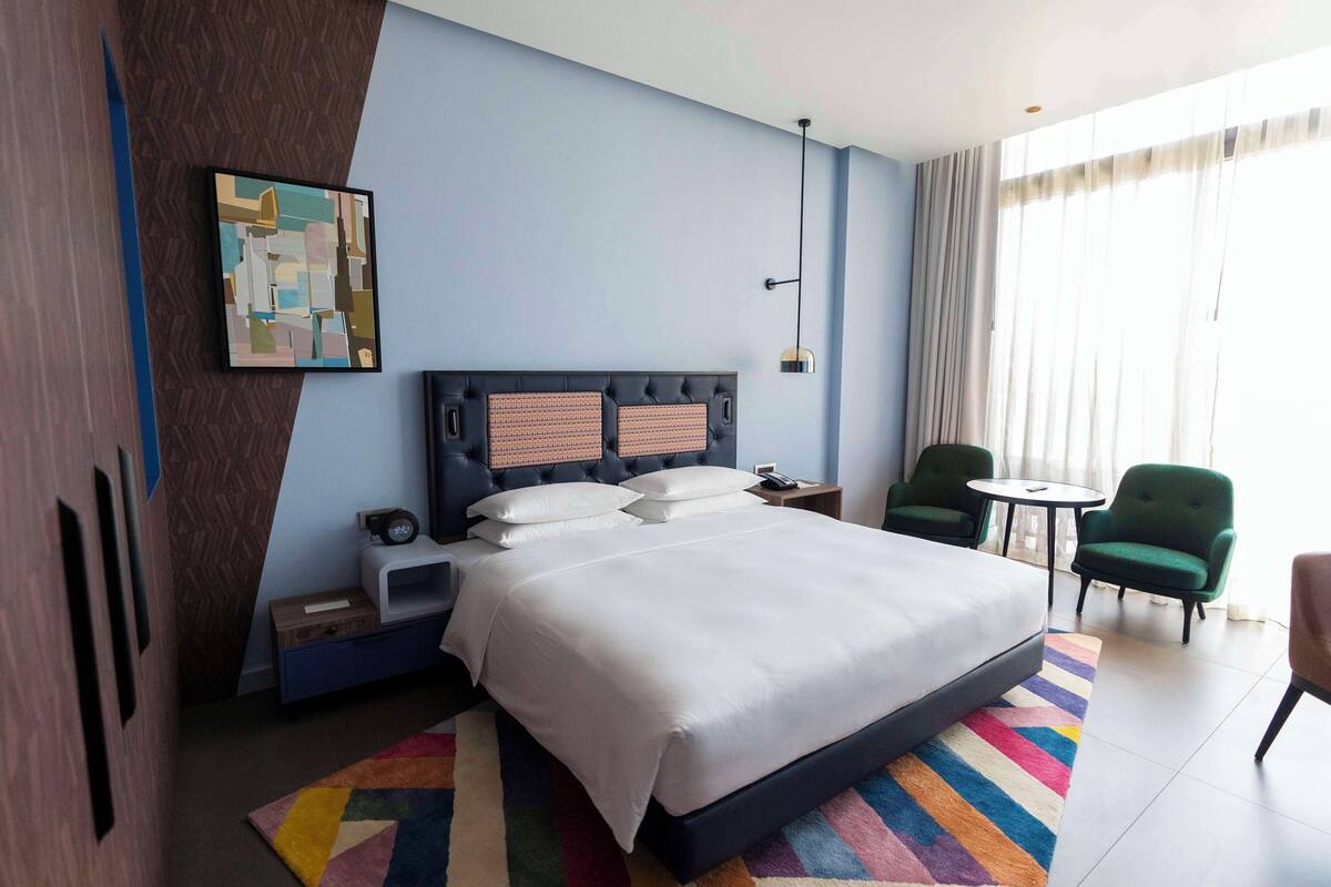 A hotel room with a large bed, a nightstand, a desk, a chair, and a window with curtains.