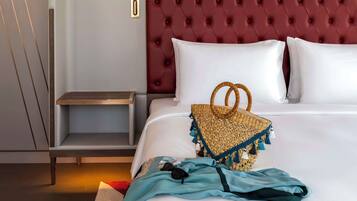 A hotel room with a large bed, a red tufted headboard, a bedside table, and a small wicker basket.