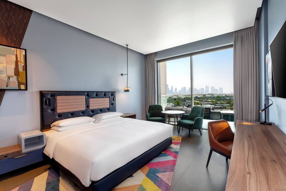 A modern hotel room with a large bed, a desk, and a view of the city skyline.