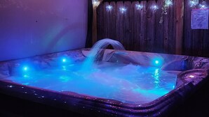 A hot tub with colorful string lights above and a wooden fence in the background.