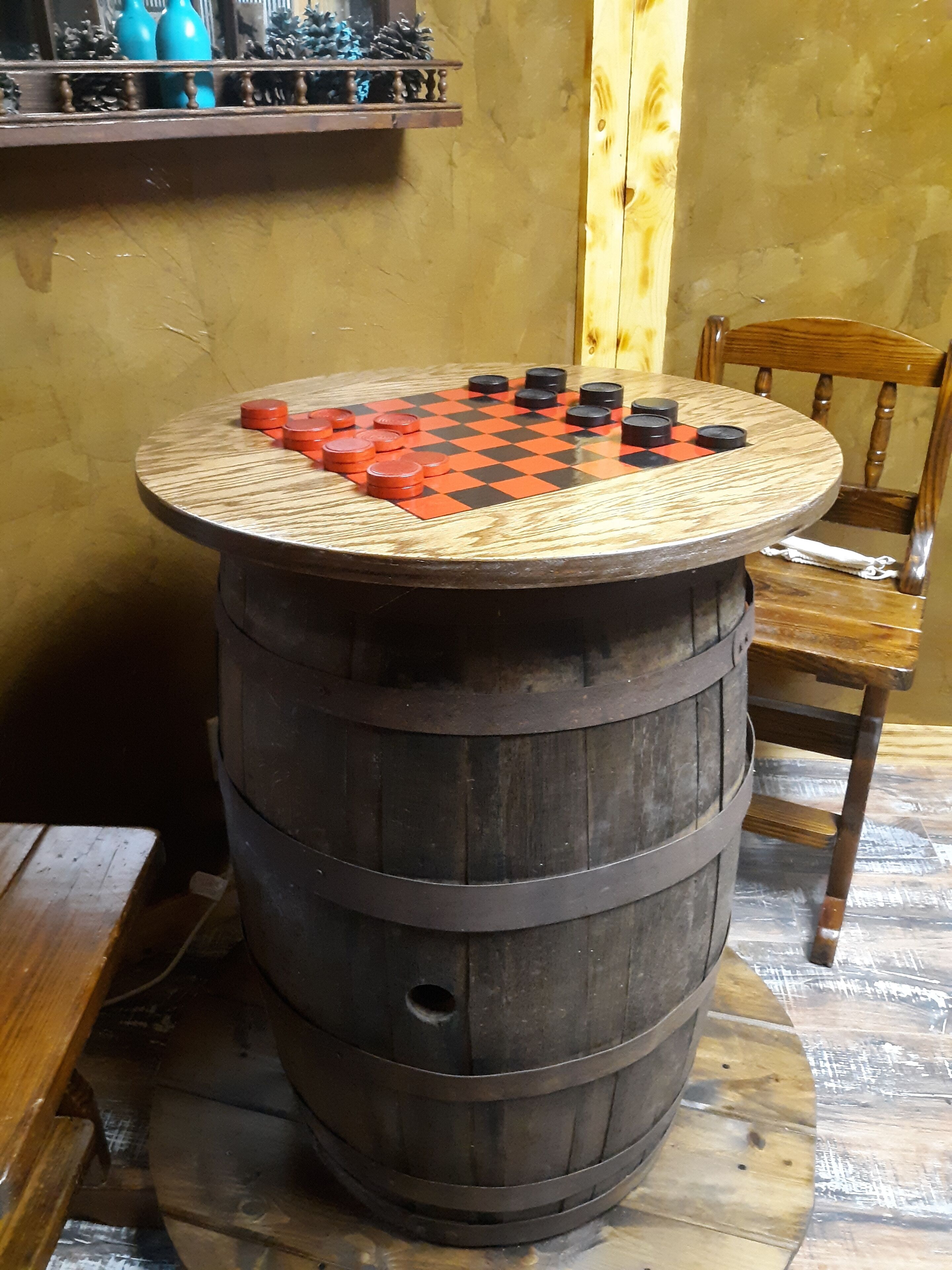 A round wooden table with a checkered chessboard on top, placed on a wooden barrel.