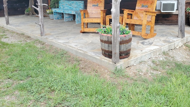 A rustic cabin with a covered porch, wooden furniture, and a large planter with flowers.
