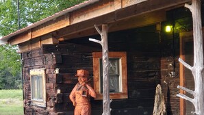 A rustic cabin with a wooden exterior, a porch, and a wooden statue of a man.
