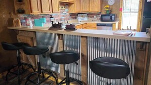 A kitchen with wooden cabinets, a microwave, a sink, and a bar area with stools.