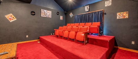 Un pequeño teatro con escalones alfombrados de rojo, hileras de asientos anaranjados y carteles en las paredes.
