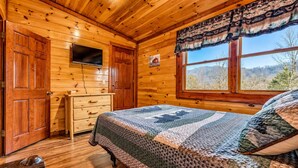 Een slaapkamer in een houten chalet, met een bed, een dressoir en een raam met uitzicht op de bergen.