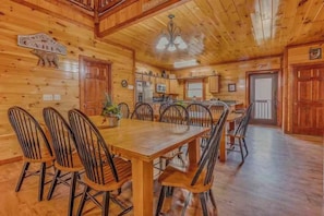 A wooden cabin interior with a dining table, chairs, a kitchen area, and a ceiling fan. - Grand Bear (Cosby)