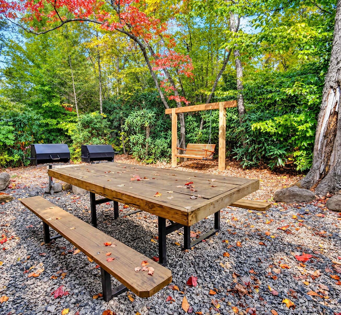 Un espace extérieur aménagé avec une table en bois et des bancs, entouré de gravier et de feuilles d’automne.