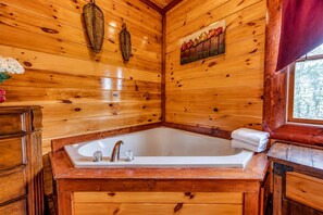 A wooden cabin interior with a large bathtub, wooden cabinets, and a window with a view of trees. - Spacious Cabin • Sleeps 30 • Pool • Hot Tub • Dogs (Cosby)