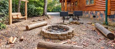 Una cabaña de troncos con chimenea de piedra, un columpio y un área de estar al aire libre techada.