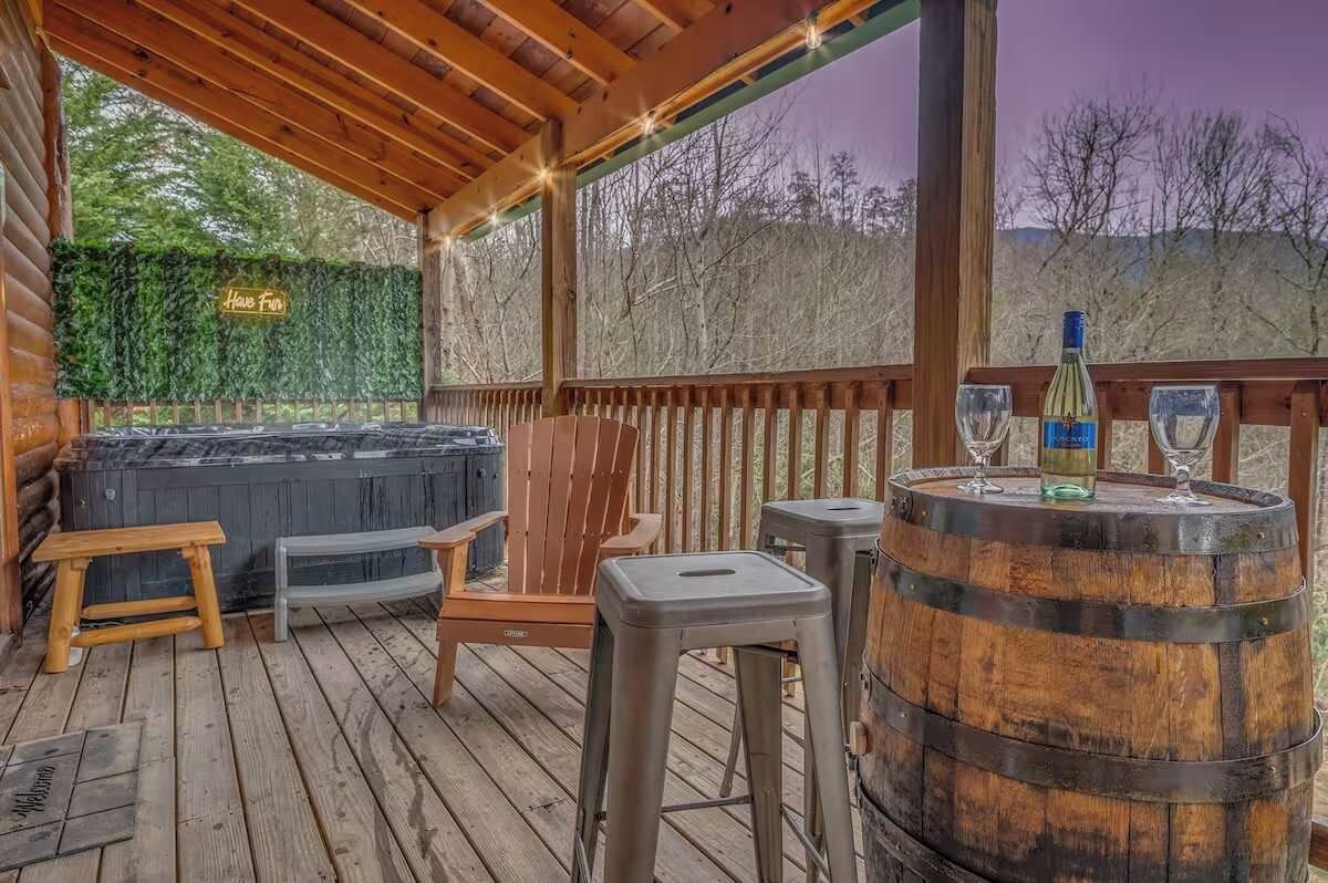 A wooden deck with a hot tub, seating, and a barrel with glasses.