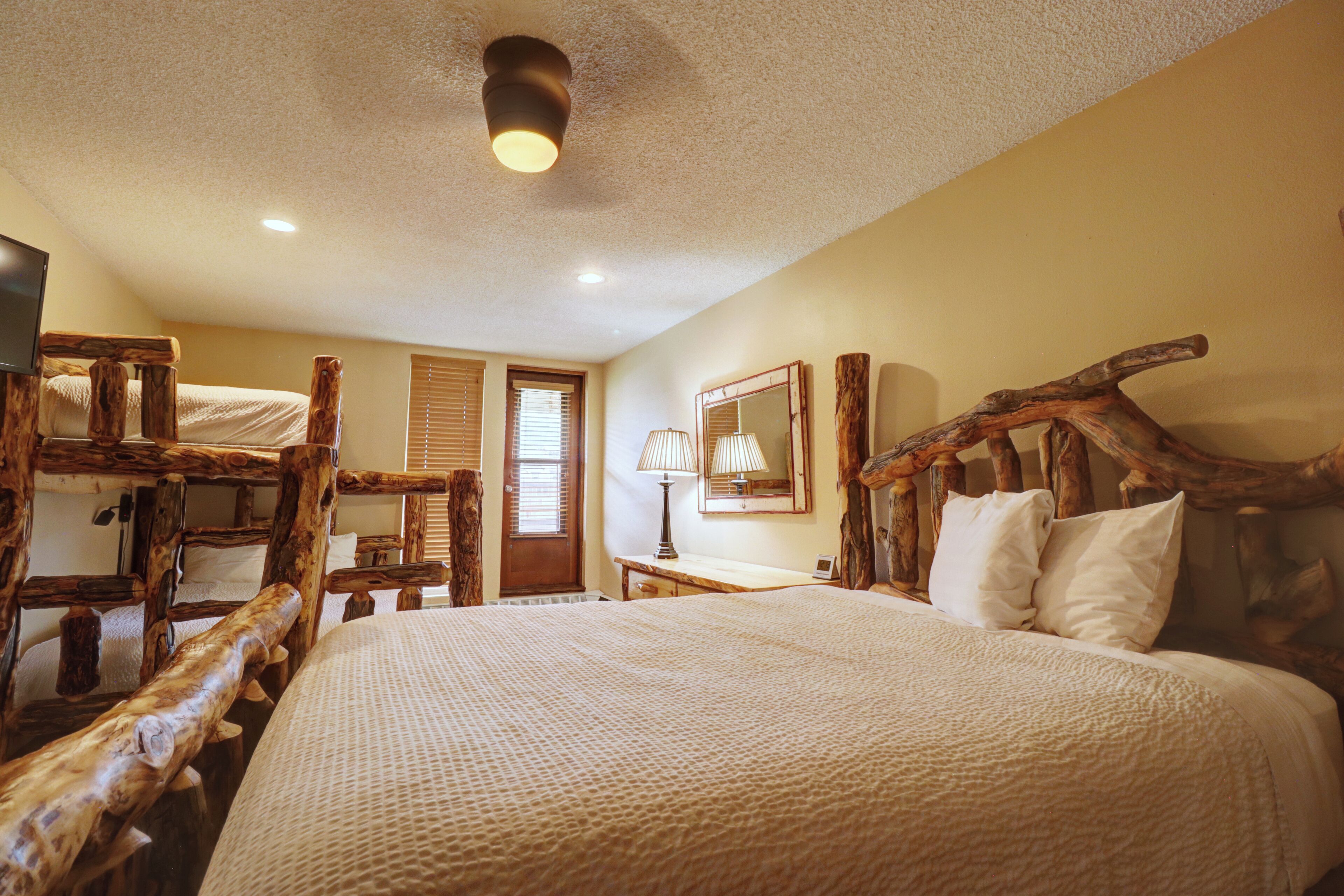 A room with a large bed, wooden headboard, a desk, a lamp, and a mirror.