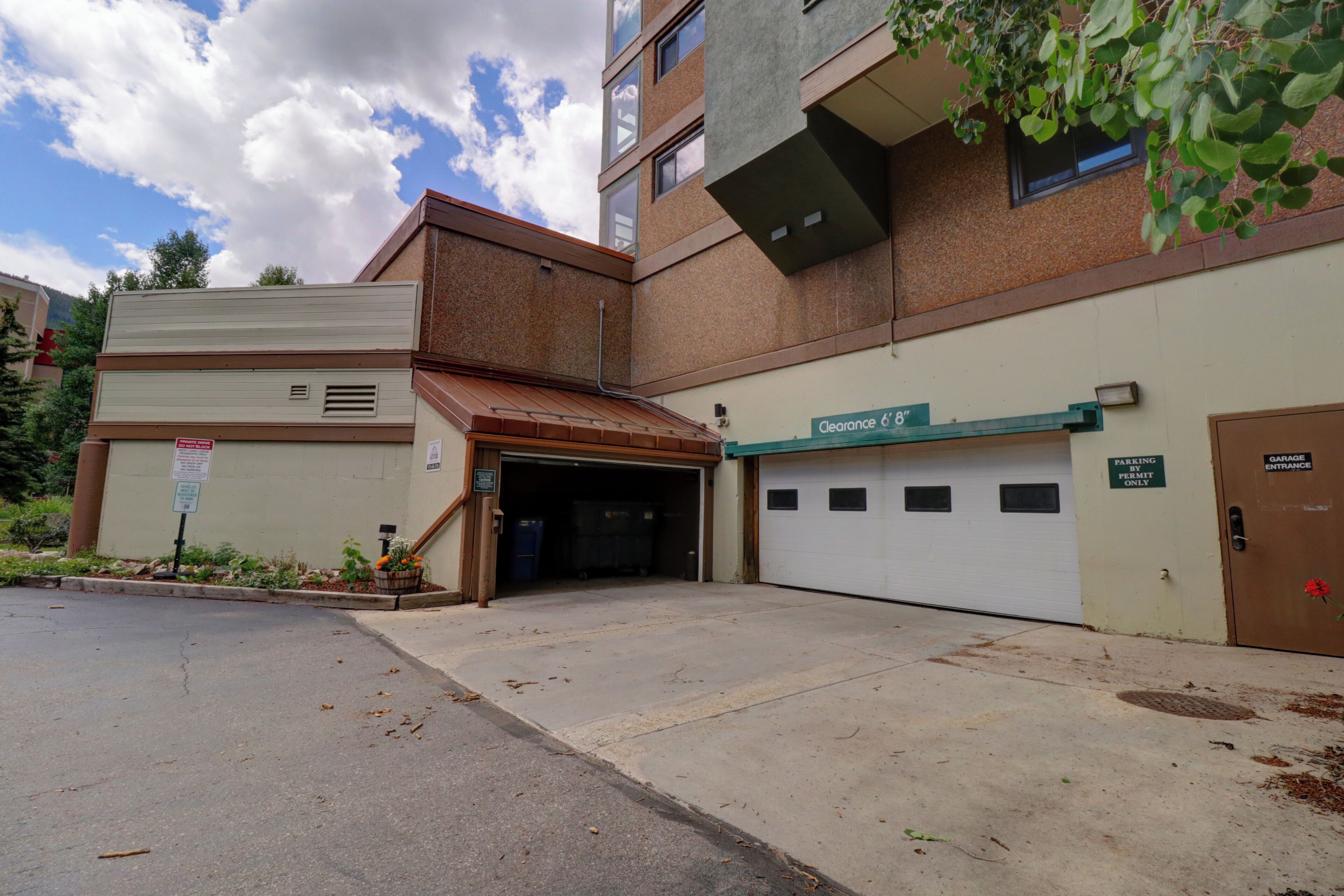 Un bâtiment avec une entrée de garage, un panneau indiquant clairement une hauteur libre de 1,80 mètre, et un panneau indiquant que le stationnement est réservé aux titulaires d’un permis.