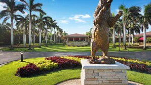 Eine Bärenstatue in einer angelegten Grünfläche mit Palmen und einem Golfplatz im Hintergrund.
