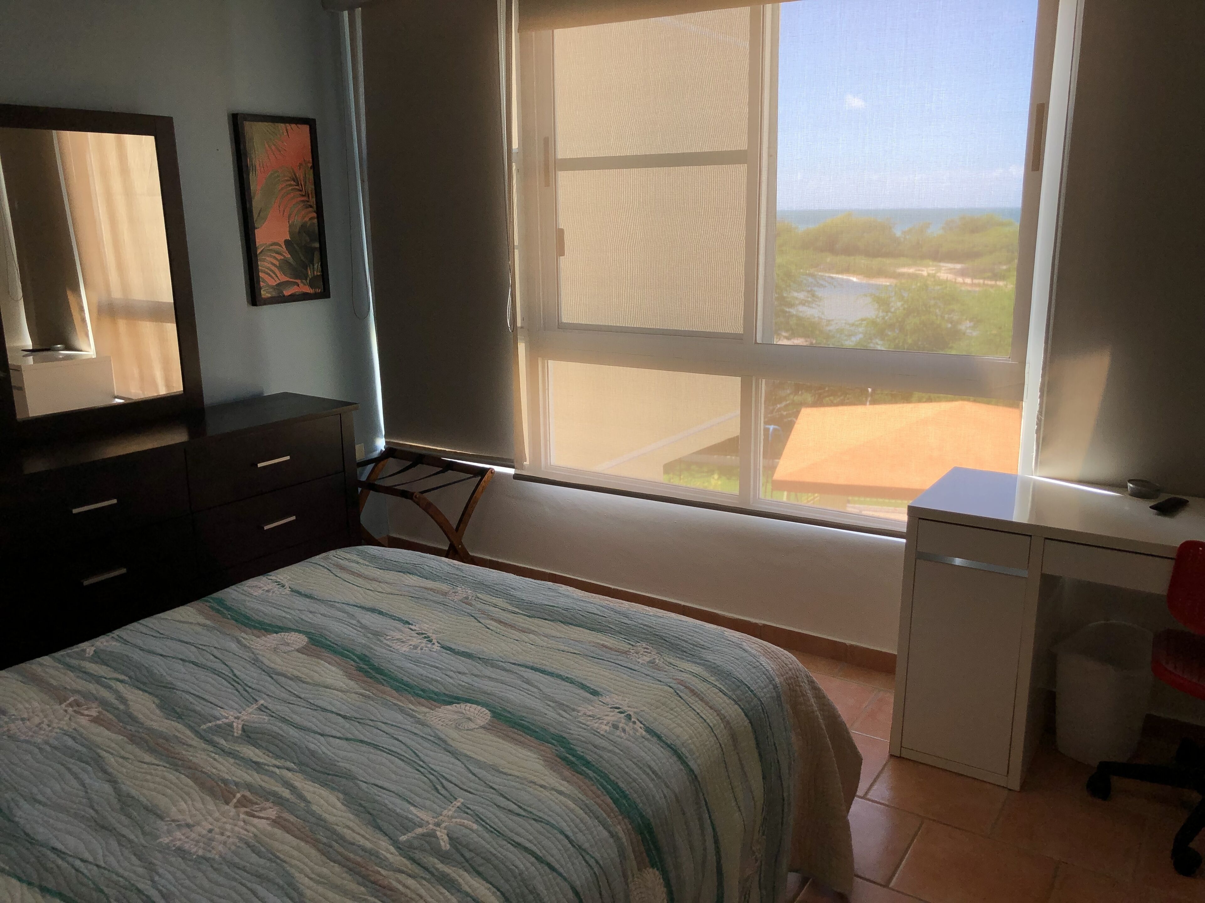 A bedroom with a bed, a desk, a chair, a window, and a dresser.
