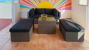 A sunburst wall mural, a black sofa, and two wicker ottomans in a bright room with large windows. - Walk-up penthouse w/breathtaking views, WiFi, A/C, free laundry, sleeps 6 (Cabo Rojo)
