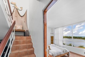 A bedroom with a large window, a staircase, and a view of a body of water. - Walk-up penthouse w/breathtaking views, WiFi, A/C, free laundry, sleeps 6 (Cabo Rojo)