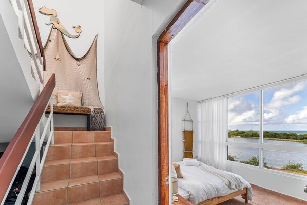 Ein Schlafzimmer mit einem großen Fenster, einer Treppe und Blick auf ein Gewässer.