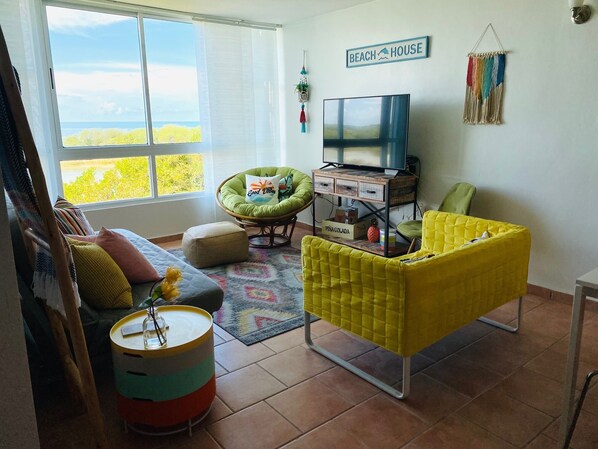 A living room with a sofa, armchairs, a TV on a wooden stand, and a view of the outdoors.