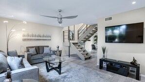 A modern living room with a grey sofa, a glass coffee table, a black entertainment unit, and a staircase leading to another level. - 3 BR Palm Springs Condo. Pool, Hot Tub. Palm Springs Art District. (Palm Springs)