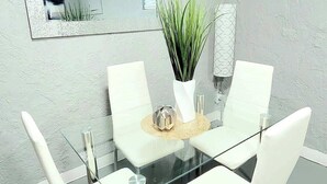 A modern dining area with a glass table, white chairs, a potted plant, and a mirror on the wall. - Walk to dining/bars/parks! Ideal for Red Rocks! (Golden)