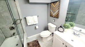 A modern bathroom with a glass shower enclosure, a toilet, a sink with a mirror, and a decorative clock.