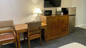 A compact hotel room with a wooden desk, a chair, a television, a microwave, and a refrigerator. - Welcome Inn (Eagle Pass)