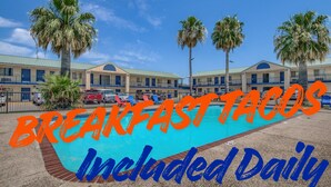 A motel with a swimming pool, palm trees, and a sign indicating breakfast tacos are included daily. - Welcome Inn (Eagle Pass)