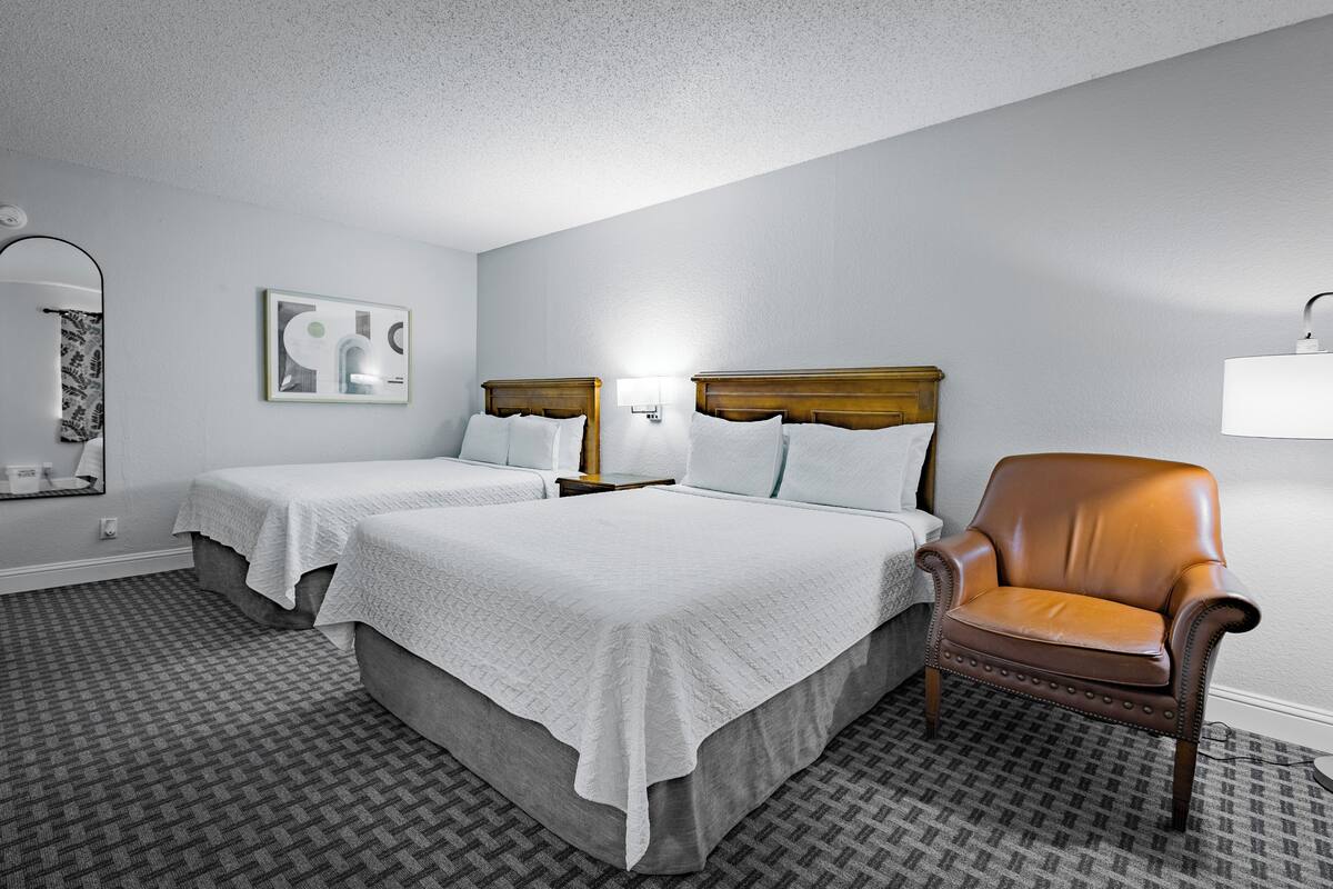 Habitación de hotel con dos camas, una silla, una lámpara y un cuadro en la pared.