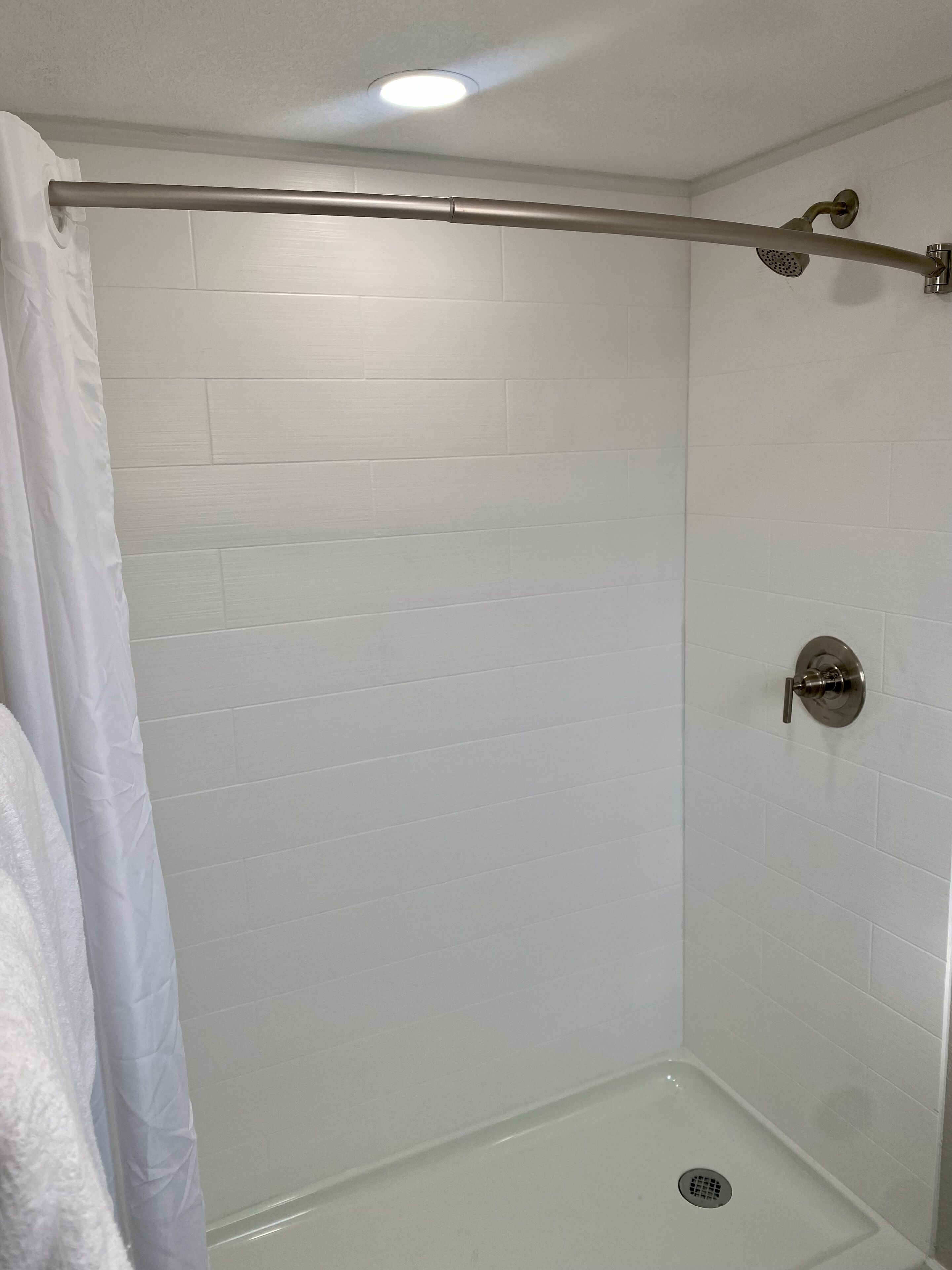 Una ducha con pared de azulejos blancos, cabezal de ducha metálico y desagüe.
