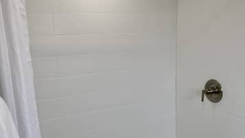 Una ducha con pared de azulejos blancos, cabezal de ducha metálico y desagüe.