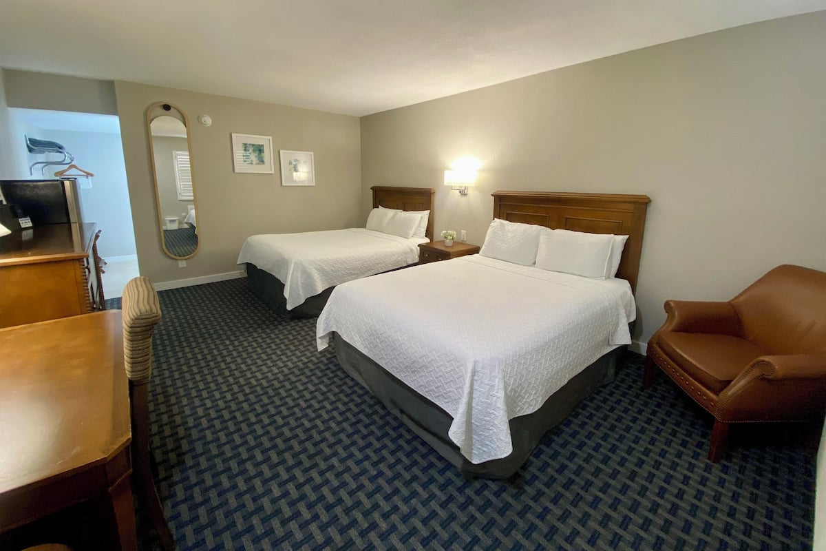 Habitación de hotel con dos camas, un escritorio, una silla, un espejo y una lámpara de pared.