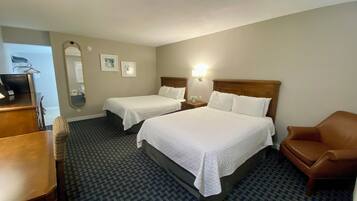 Habitación de hotel con dos camas, un escritorio, una silla, un espejo y una lámpara de pared.
