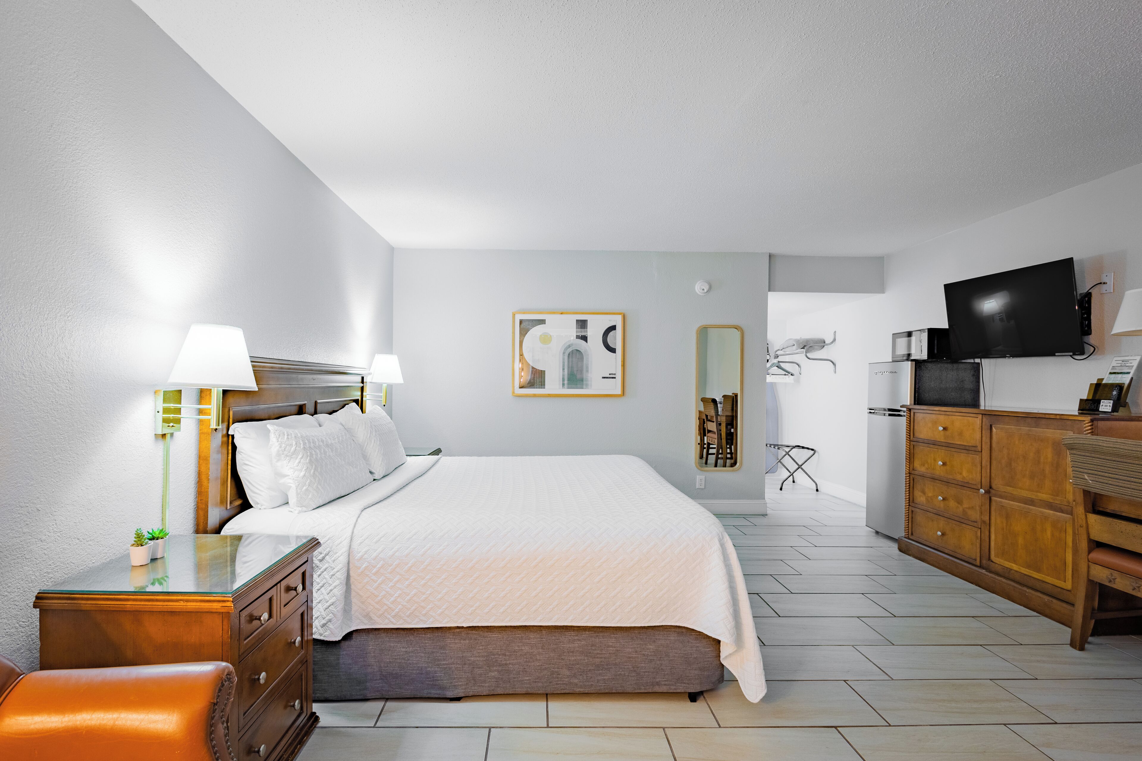 A modern hotel room with a large bed, bedside tables, a desk, a TV, and a mirror.