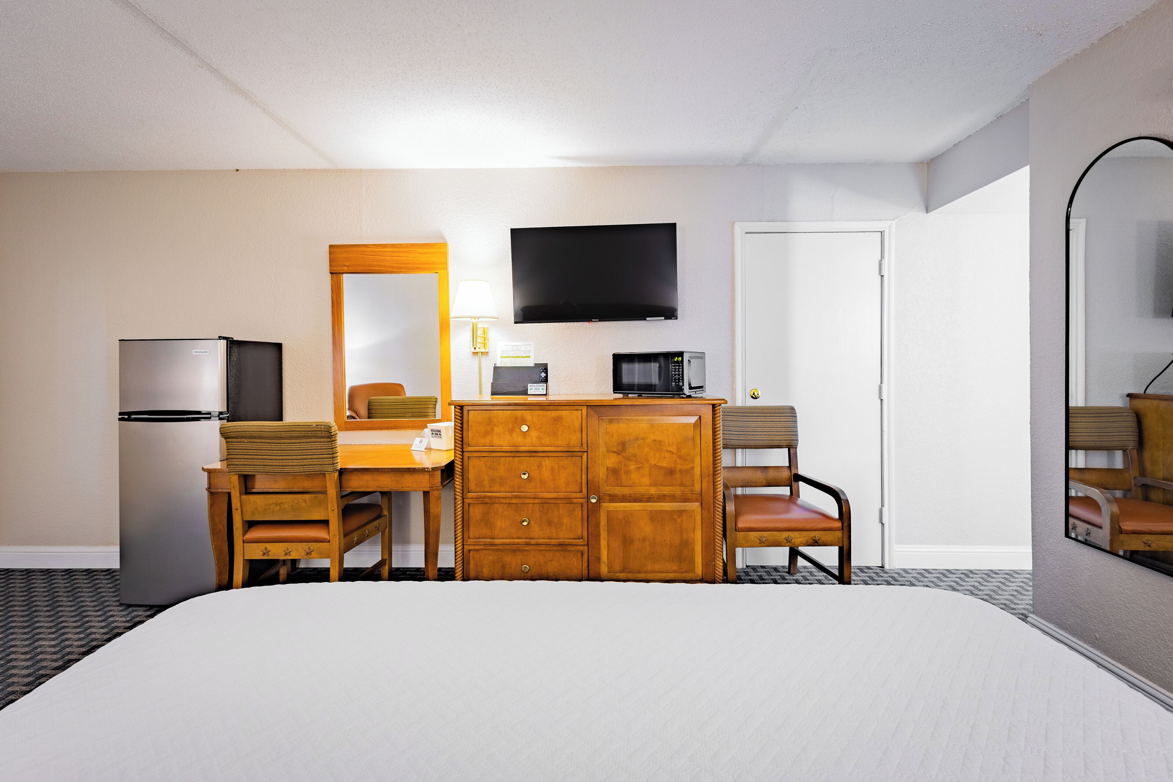 A hotel room with a bed, a desk with a chair, a dresser, a television, a microwave, and a refrigerator.
