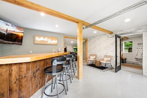 A modern bar area with wooden beams, bar stools, a neon sign, and a view of the sunset.