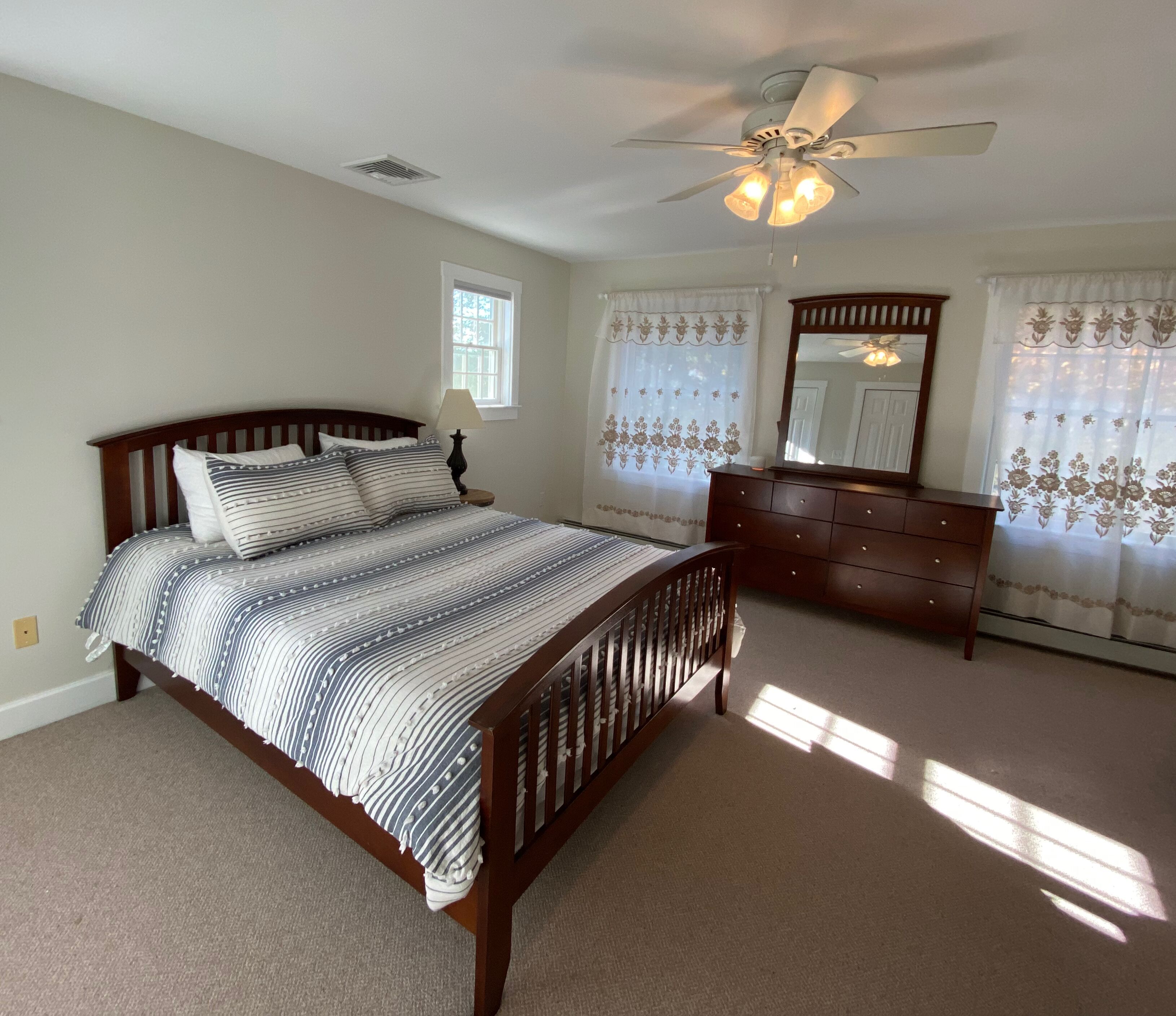 A bedroom with a bed, dresser, mirror, and ceiling fan.
