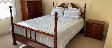 Quarto com cama de dossel de madeira, mesa de cabeceira, cômoda e janela com cortinas de renda.