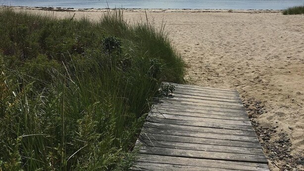Een houten looppad dat naar een zandstrand leidt, onder een heldere lucht.