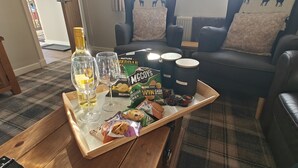 A wooden tray with snacks, McCain's products, and wine glasses on a table in a living room with a plaid carpet and a black leather couch. - Ben Lomond Cottage - Loch Lomond and Arrochar Alps (Arrochar)