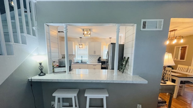 A modern kitchen with a central island, two bar stools, and a view into the dining area.