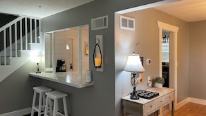 A modern kitchen with white bar stools, a coffee station, and a dining area with a table and chairs.