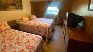 A room with two beds, a desk with a television, a painting on the wall, and a window with curtains. - Beautiful Water Front Cabins (Georgetown)