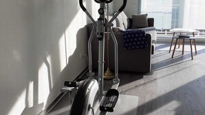 Een sportruimte met een elliptische machine, een uitslaande bureau en een bank in een zonnige kamer met een groot raam.
