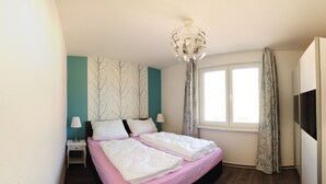 Een slaapkamer met een bed, nachtkastjes, een lamp, een plafondlamp, een raam met gordijnen en een televisie.