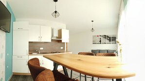 Een moderne keuken met witte kasten, een houten eettafel en bruine stoelen. Boven de tafel hangen hanglampen.